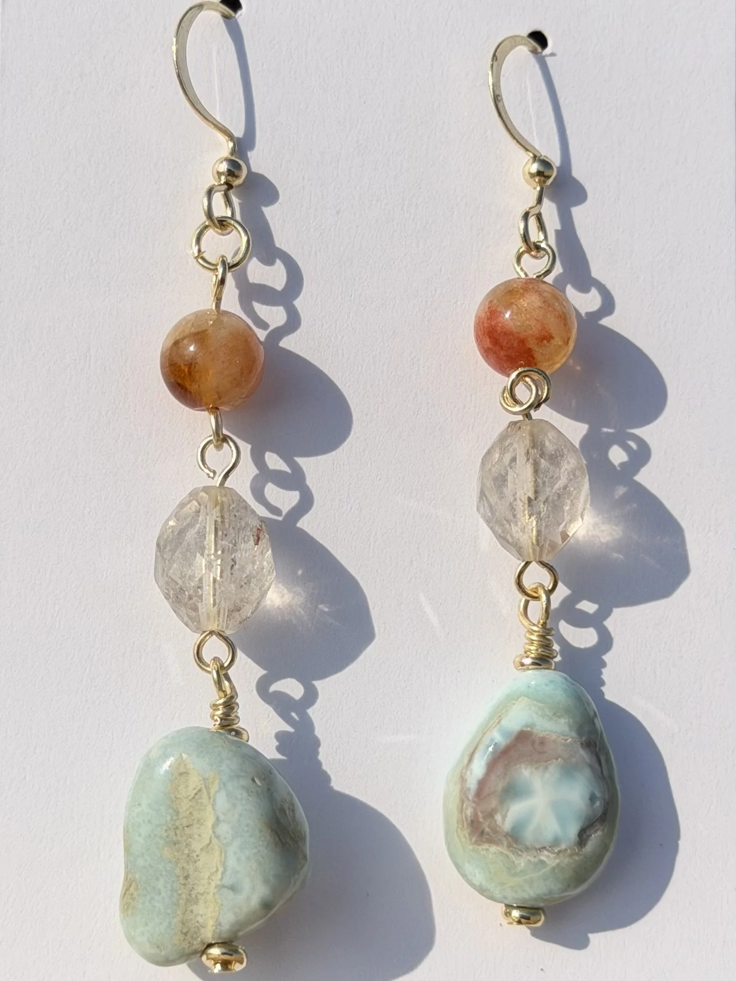 Close-up of handmade gemstone drop earrings featuring warm orange, translucent and pale blue natural stones.
