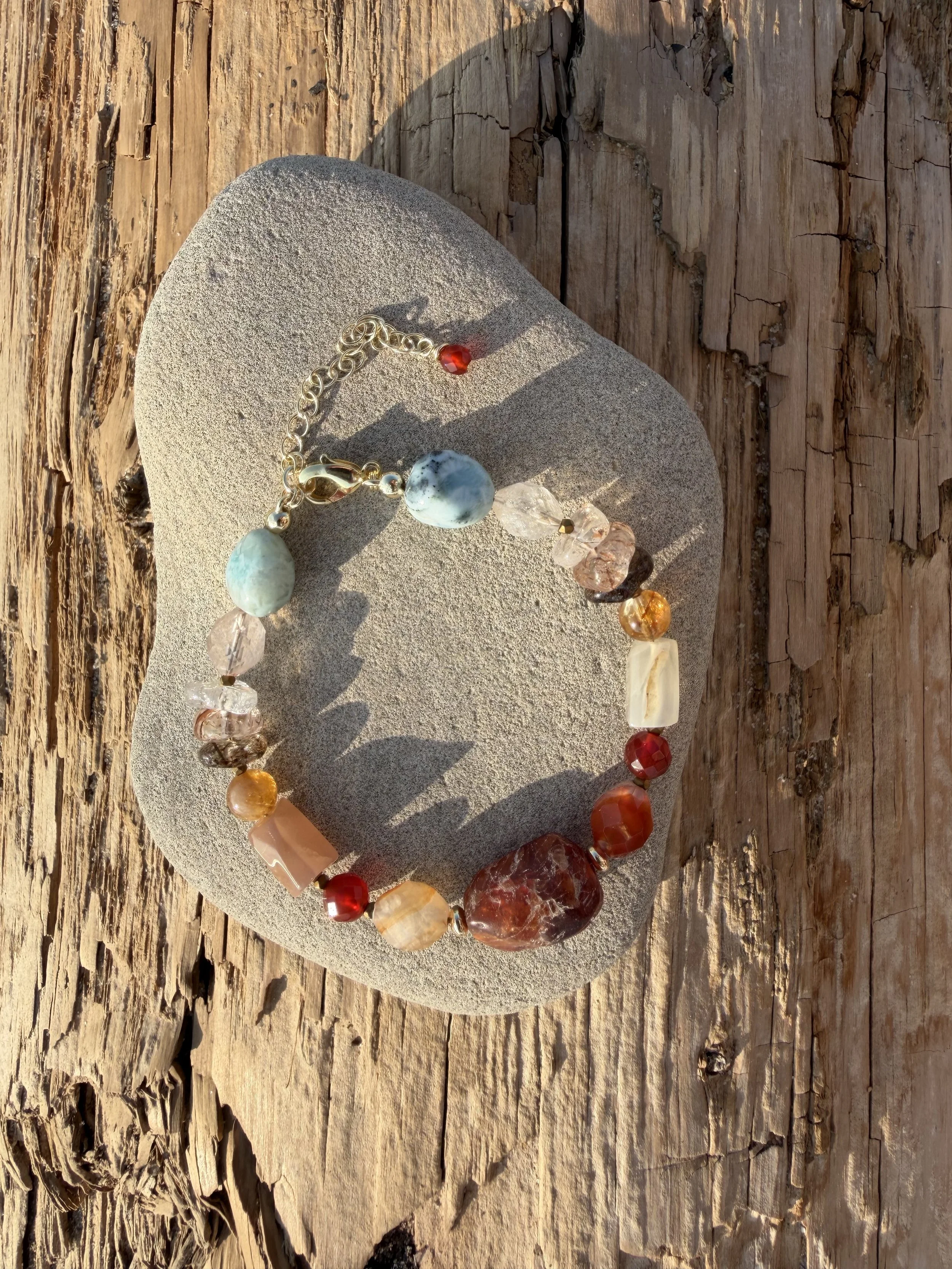 Handmade gemstone bracelet with blue, red, amber and translucent natural stones displayed on a smooth stone.