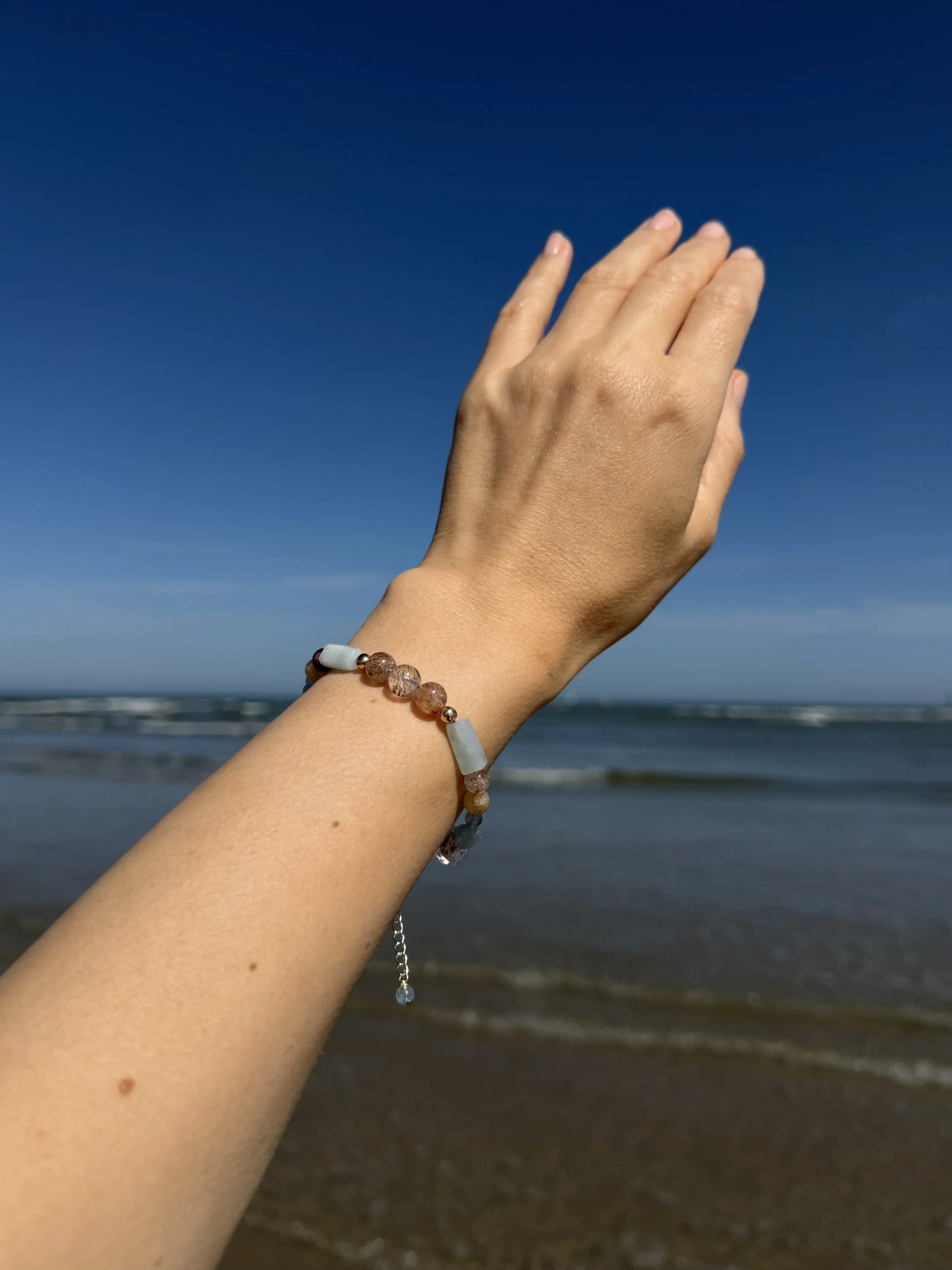 Handmade gemstone bracelet worn on the wrist at the beach, showing the fit and adjustable chain.