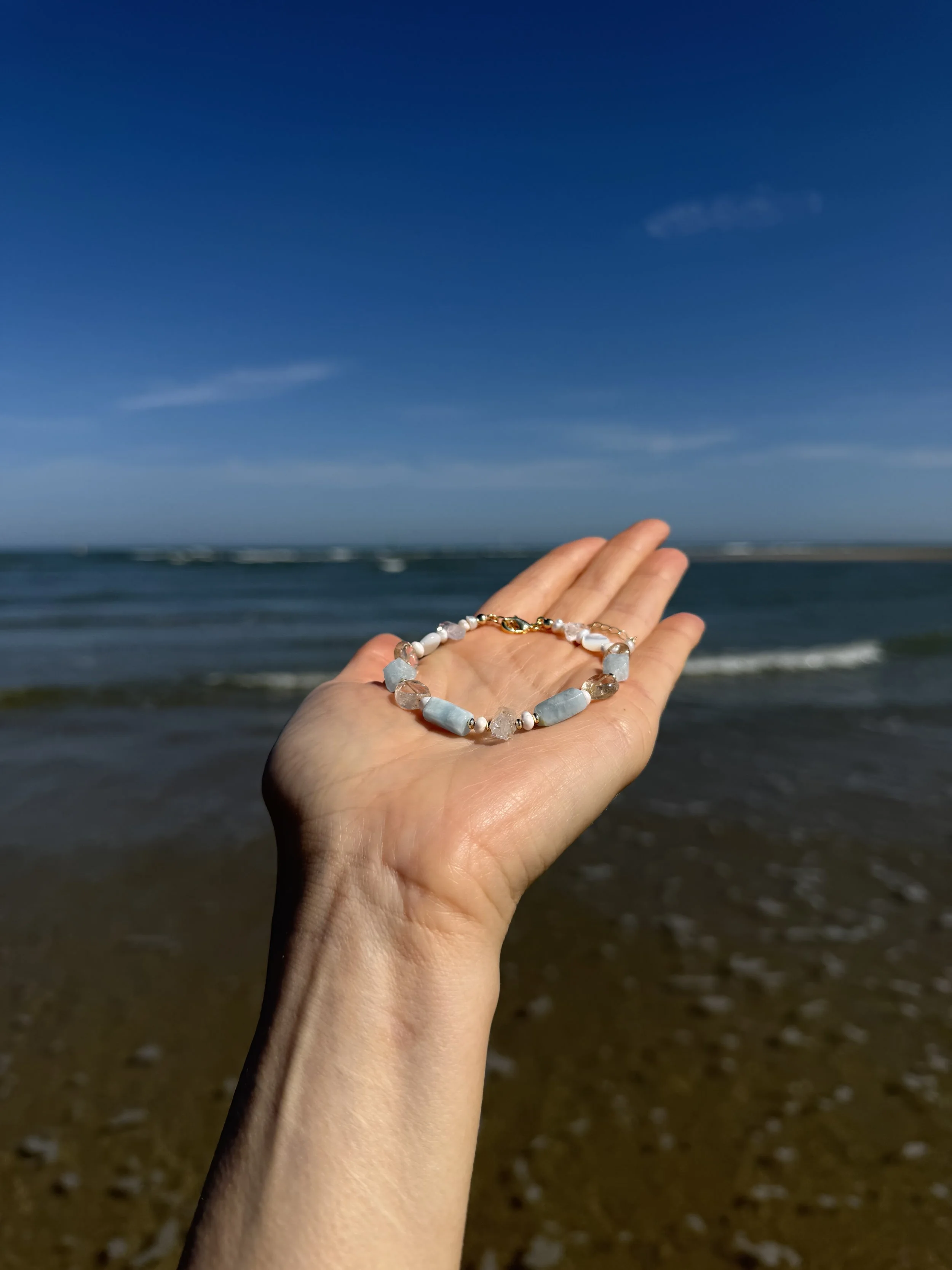 Handmade gemstone bracelet displayed in an open hand with the sea in the background.