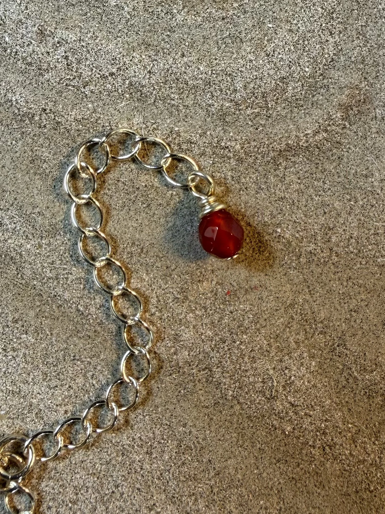 Close-up of the adjustable chain finished with a small red gemstone bead.