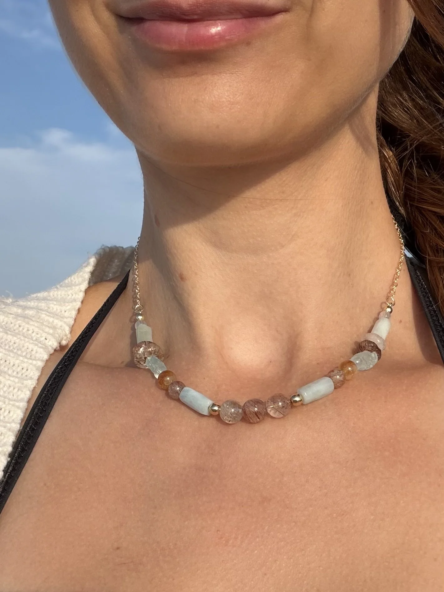 Handmade gemstone necklace with soft blue, white and warm-toned natural gemstones worn at the beach.