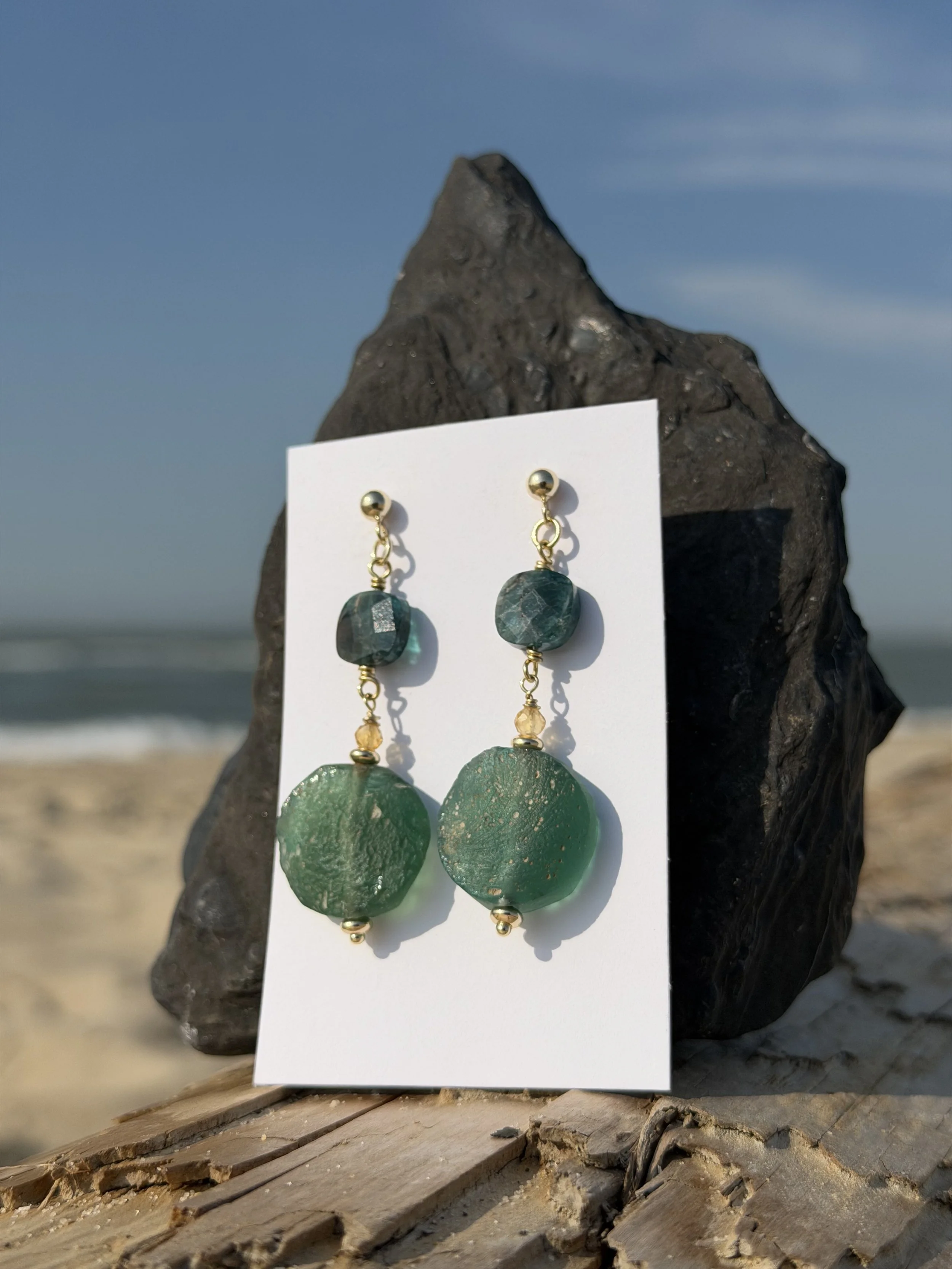 Handmade green gemstone drop earrings displayed on a white card against natural stone.