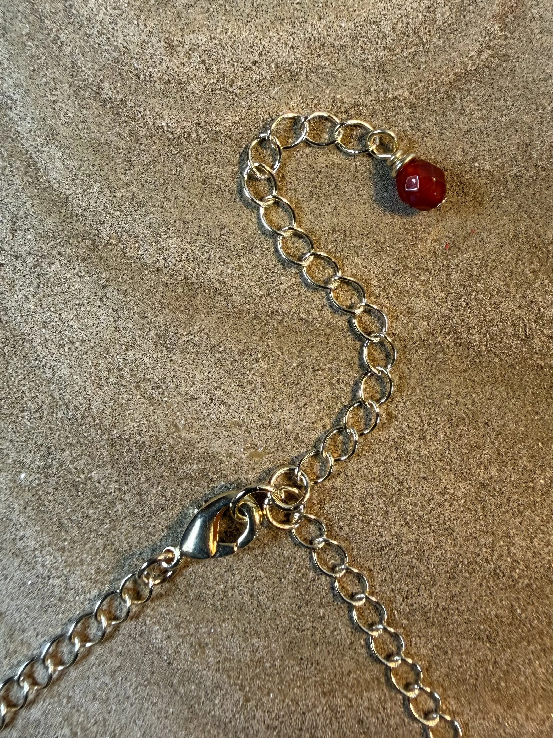 Close-up of the gold clasp, adjustable chain and red gemstone detail of a handmade necklace.