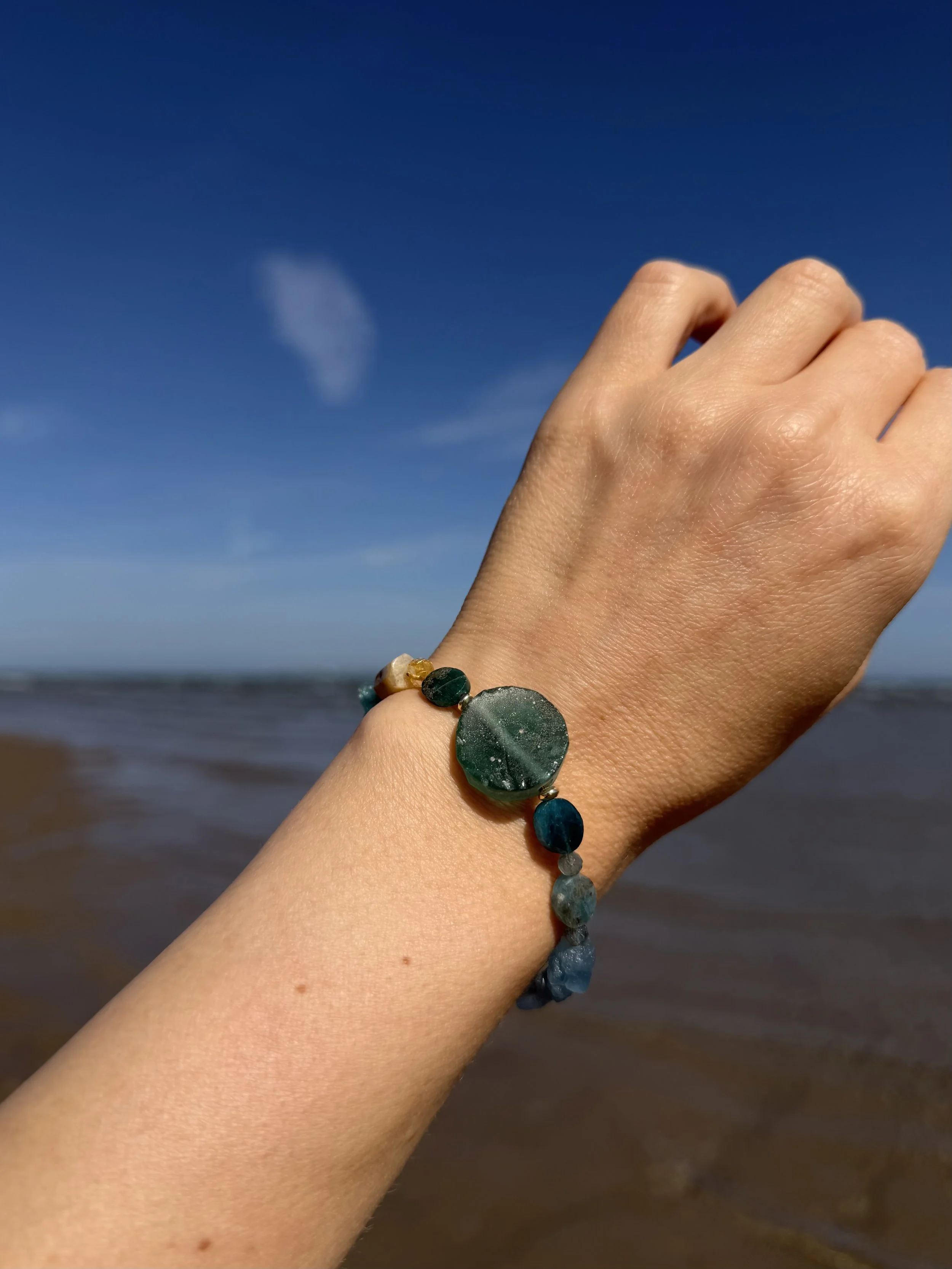 Handmade green and blue gemstone bracelet worn on the wrist by the sea.