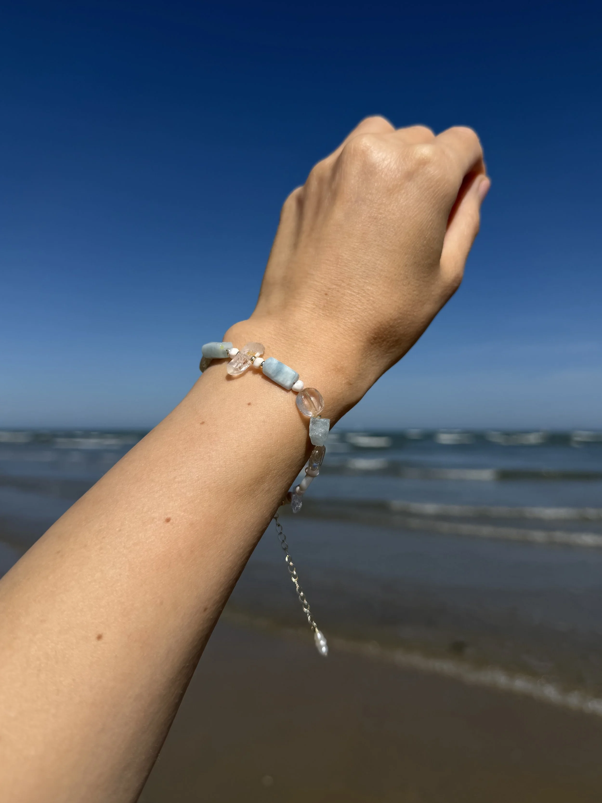 Handmade gemstone bracelet with pale blue and white stones worn on the wrist at the beach.