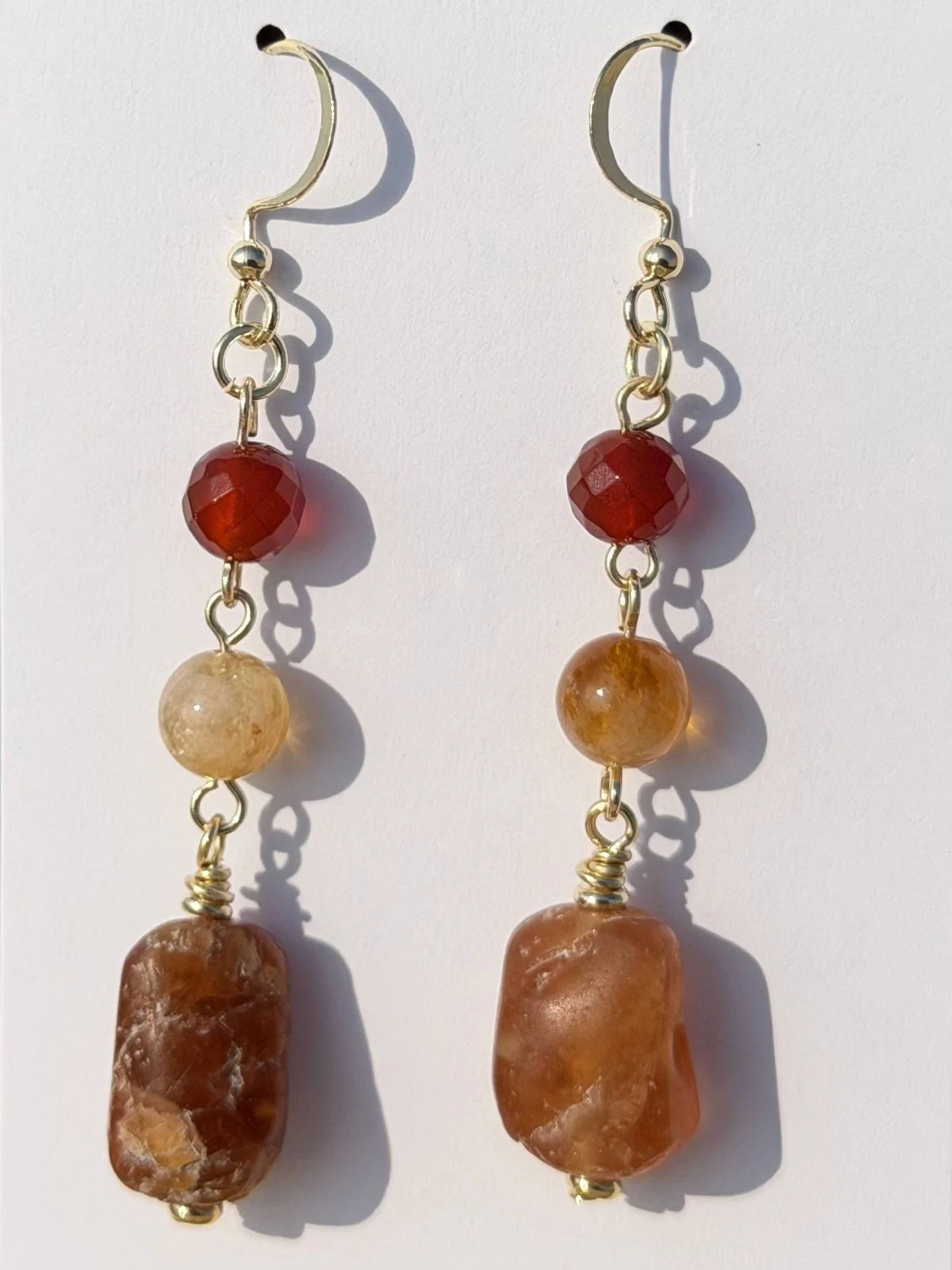 Close-up of handmade gemstone drop earrings featuring red, golden yellow and warm brown natural stones.