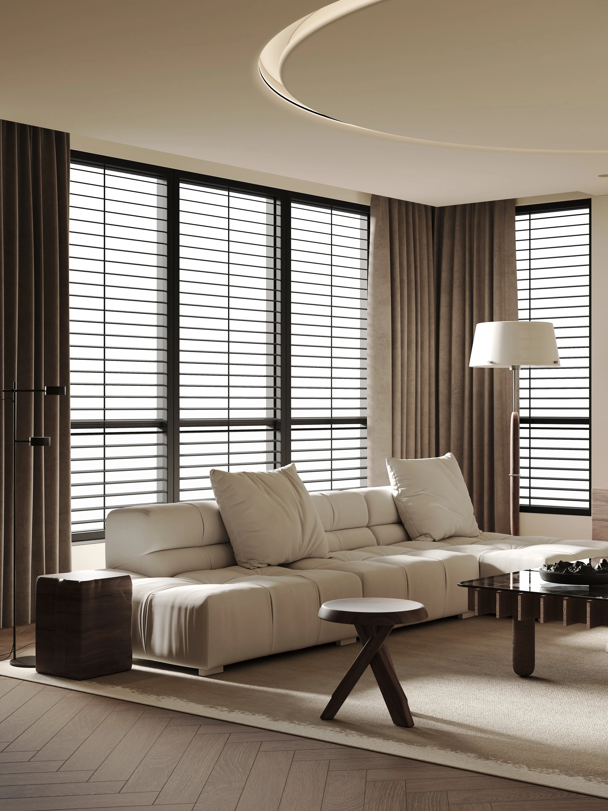 Modern living room with large windows covered by dark curtains, a white couch with pillows, a dark wooden side table, a contemporary floor lamp, a glass coffee table, and light wood herringbone flooring.