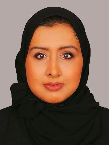 A woman wearing a black headscarf with a neutral gray background.