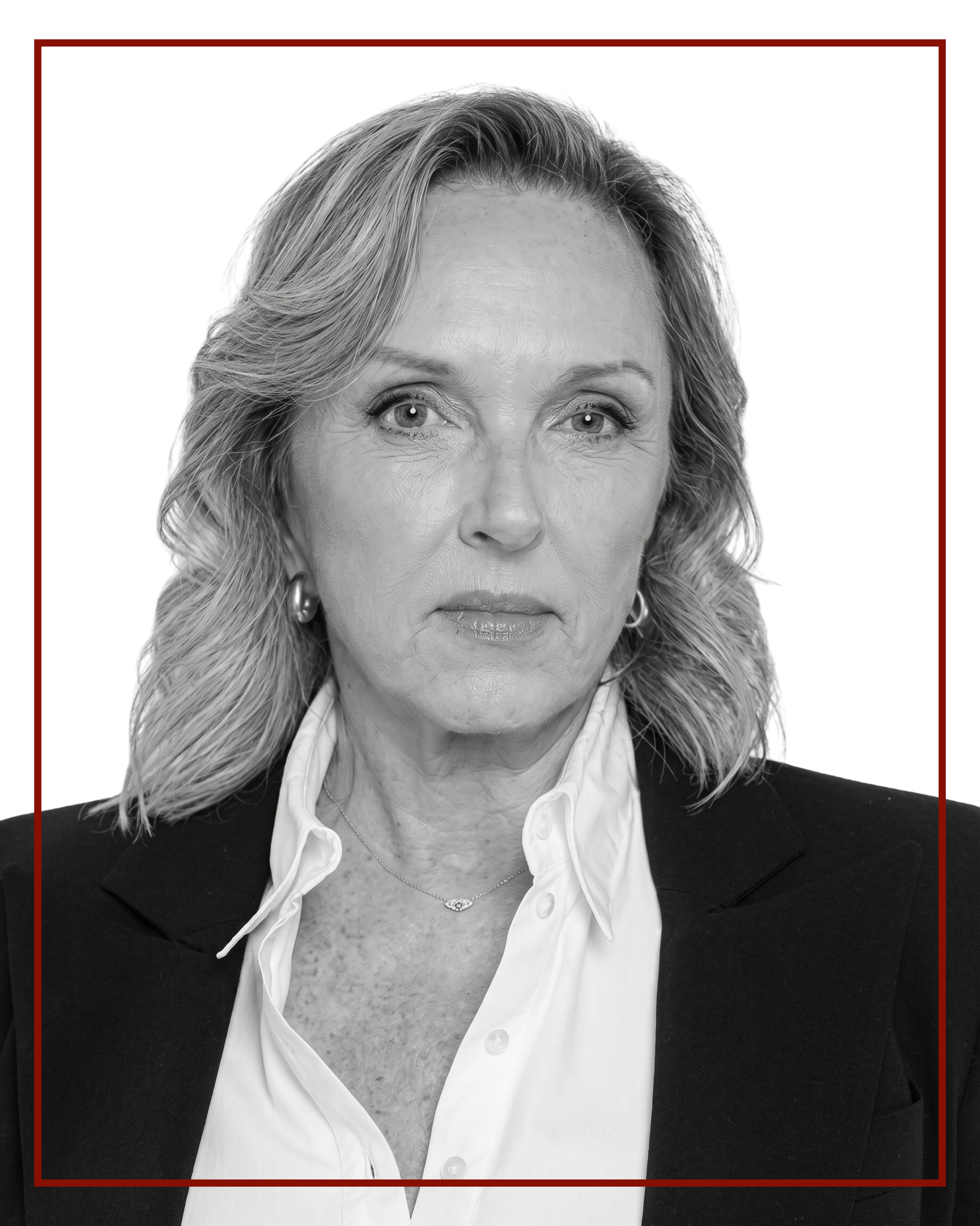Black and white portrait of a woman with blonde hair, wearing a white shirt and blazer, with jewelry, looking directly at the camera.