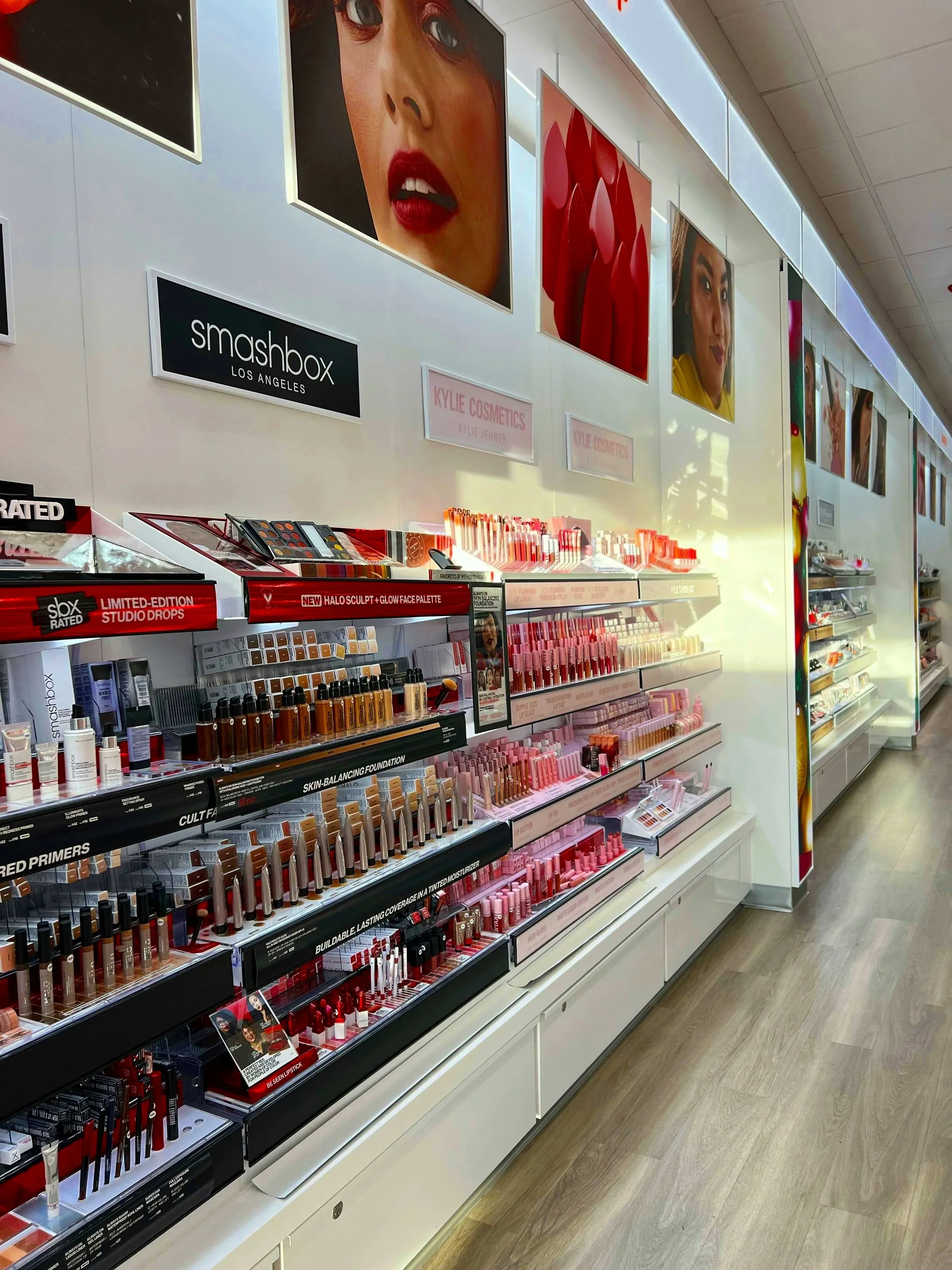 Display of makeup products, including lipsticks and foundation, at a cosmetics store with large posters of women on the wall
