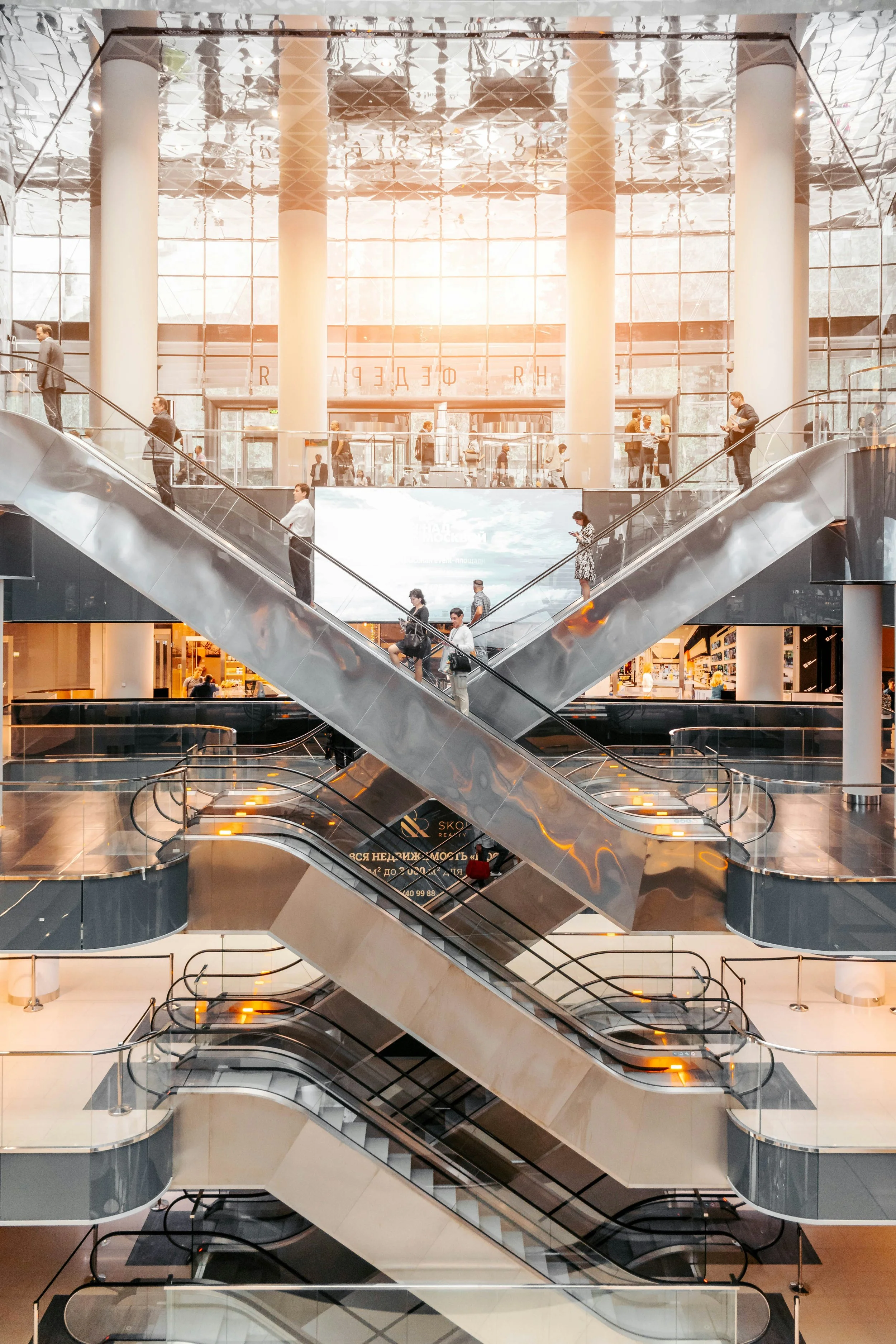 Multiple escalators inside a modern shopping mall connecting different floors with glass railings and a spacious, bright interior.