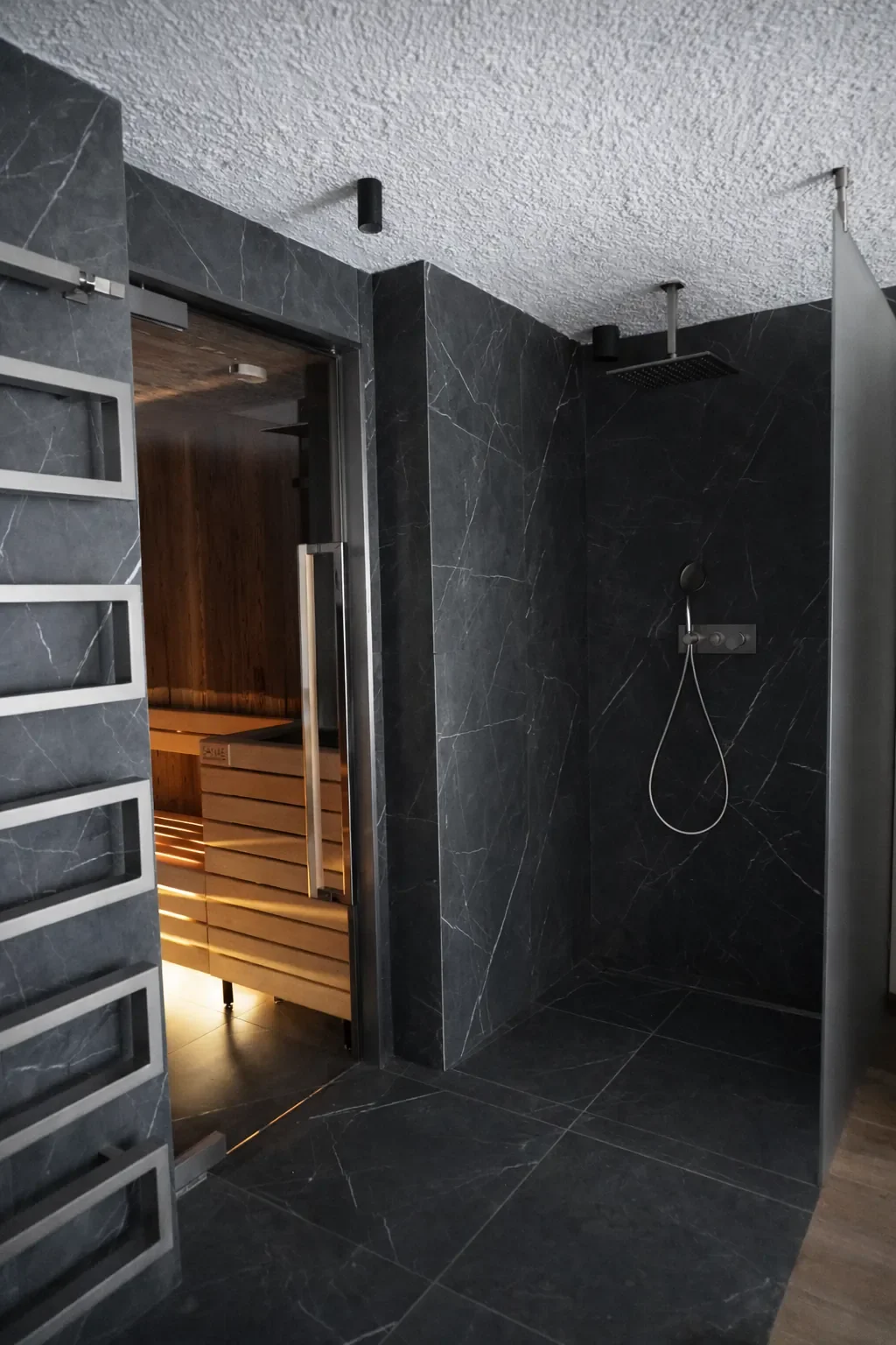 Doccia aperta con pareti in marmo nero, soffitto in textured bianco, con pioggia shower e manopola per acqua, enigma senza porte, vicino a sauna in legno