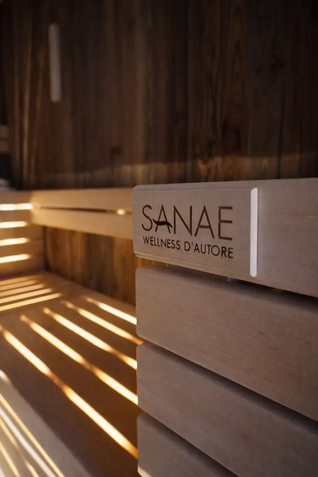 Segnale in legno con scritta 'SANAÉ WELLNESS D'AUTORE' all'interno di una sauna in legno.