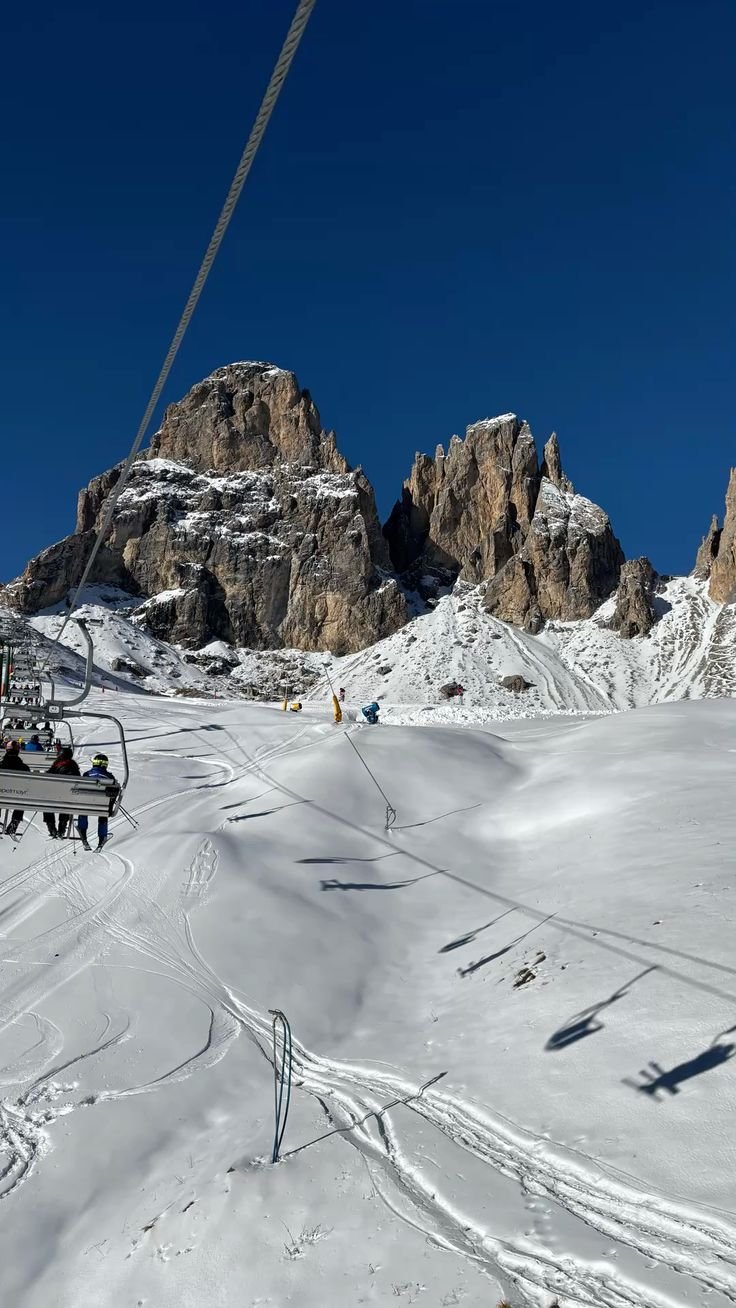 Pista da sci con alcune persone e seggiovie in montagna, con rocce e neve, sotto un cielo terso