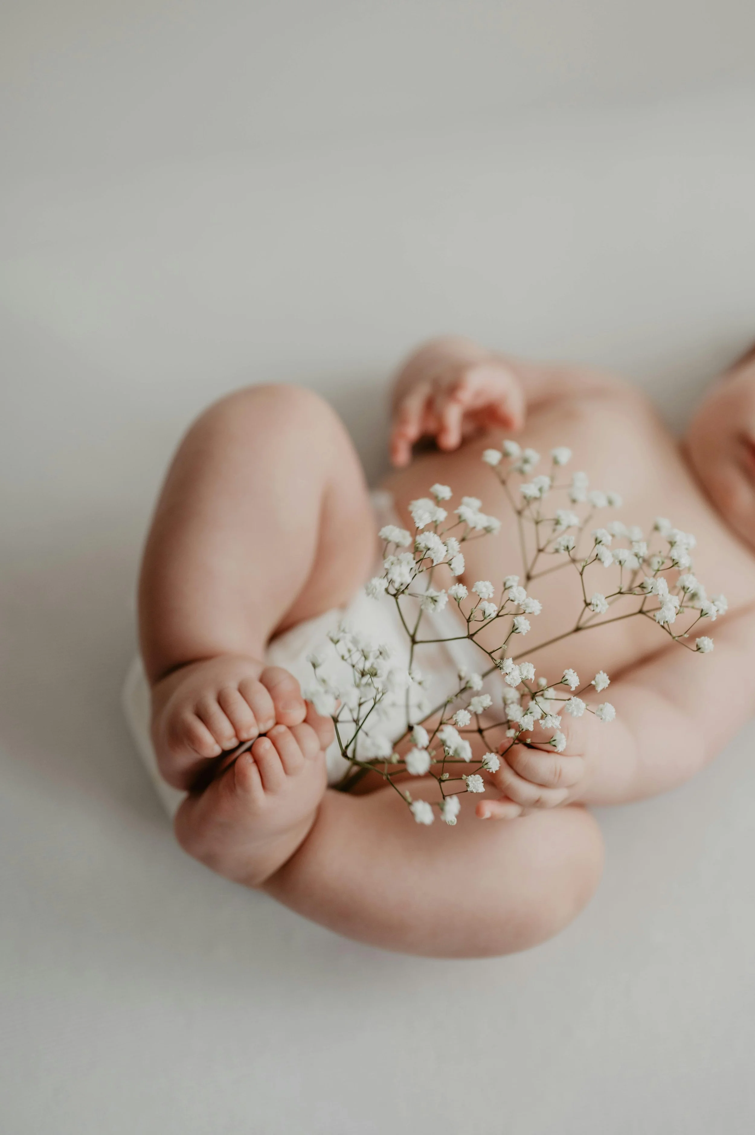 Close-up of a baby holding a sprig of small white flowers, with part of their face and body visible.