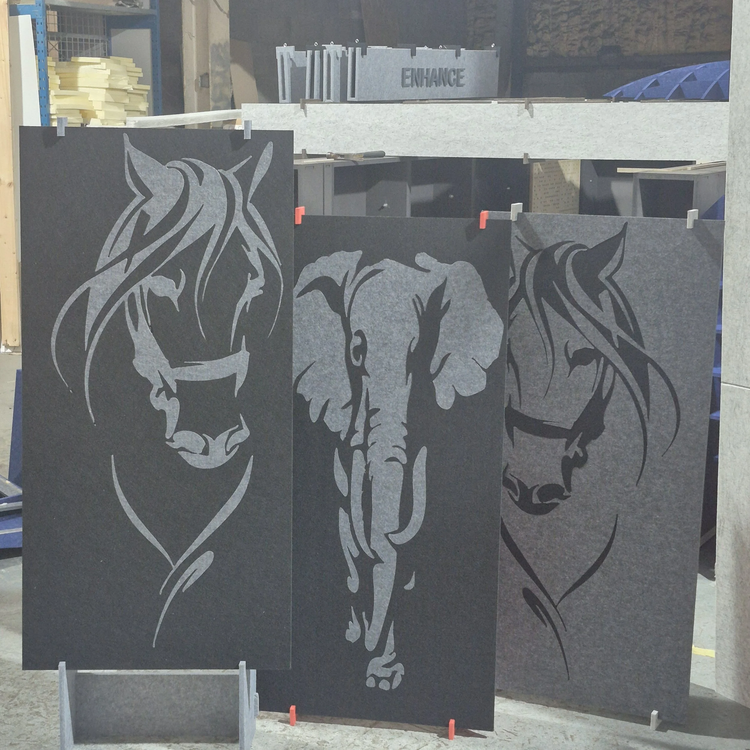 Black Acoustic panels with a lion's head and mane design cutouts, propped up vertically in a storage area, with foam pads and construction tools visible nearby.
