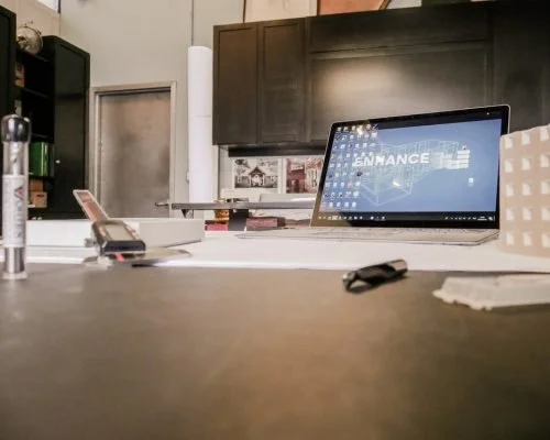 A laptop on a kitchen counter with a desktop wallpaper that says 'ENHANCE'.