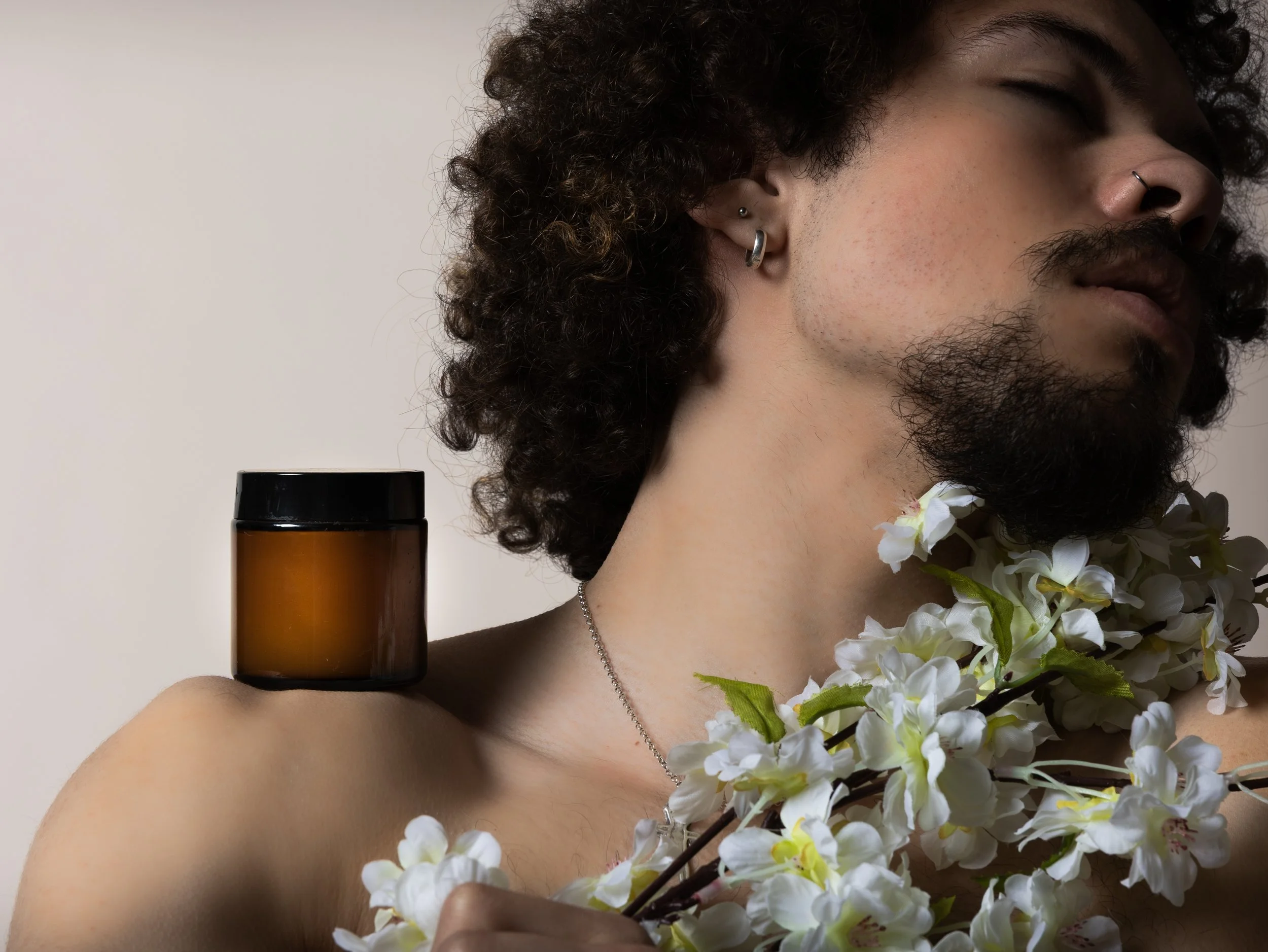 En man med krulligt hår och piercingar i örat, omgiven av vita blommor, konstnärligt foto.