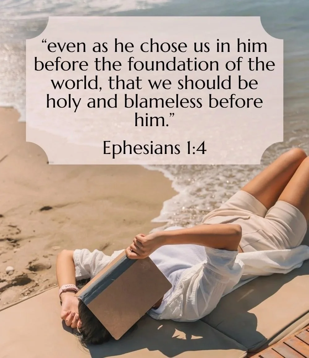 A person lying on their side on a lounge chair on the beach, reading a book, with an overlay of a Bible verse from Ephesians 1:4.