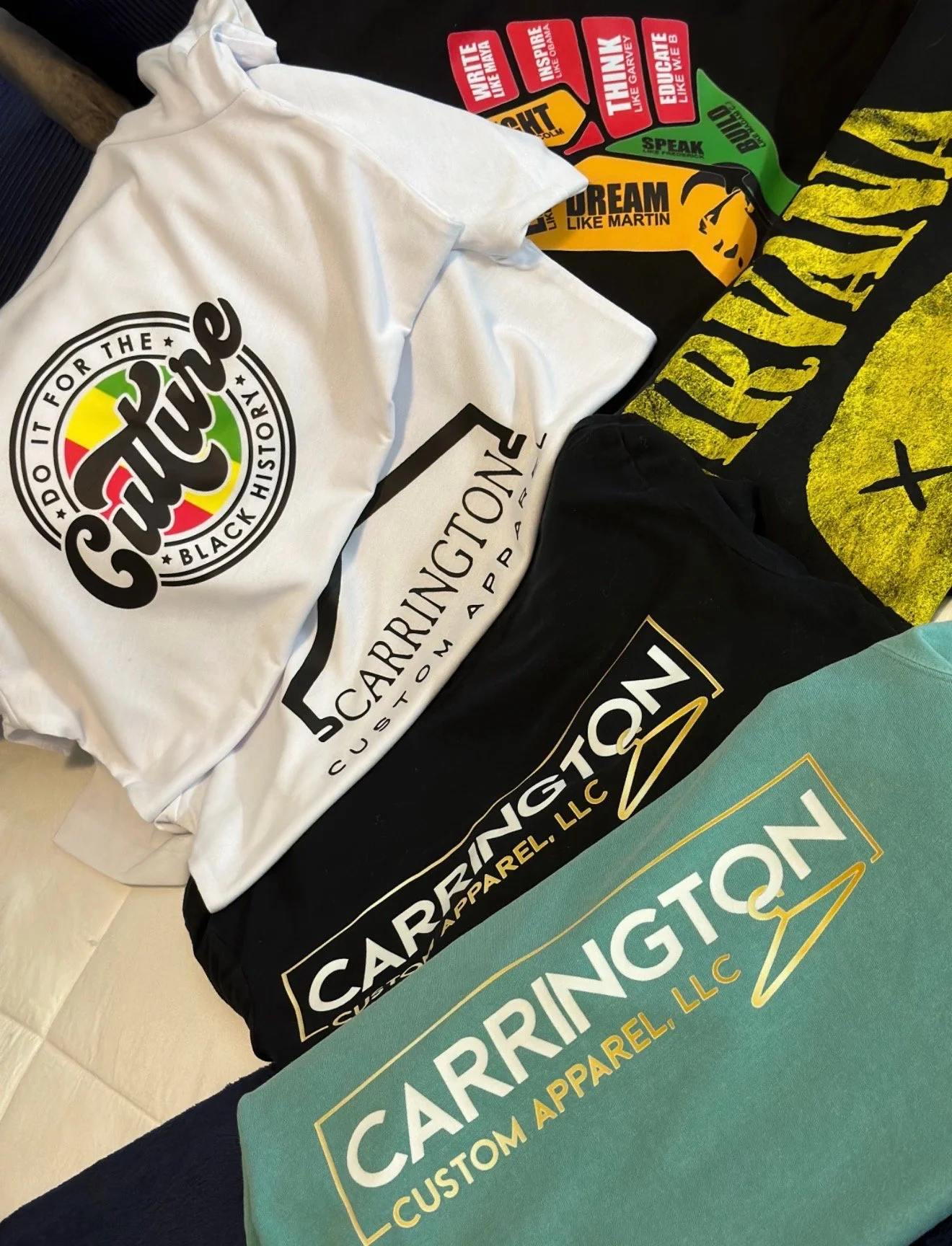 Various T-shirts and clothing items from different brands, including Carington, Catchy, and others, laid out on a surface.