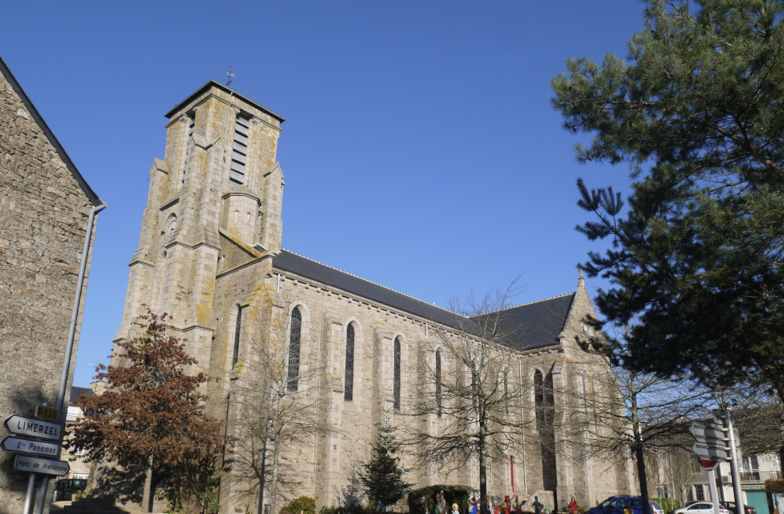 Vue d'une ancienne église en pierre avec une tour, arbres autour et un ciel clair.