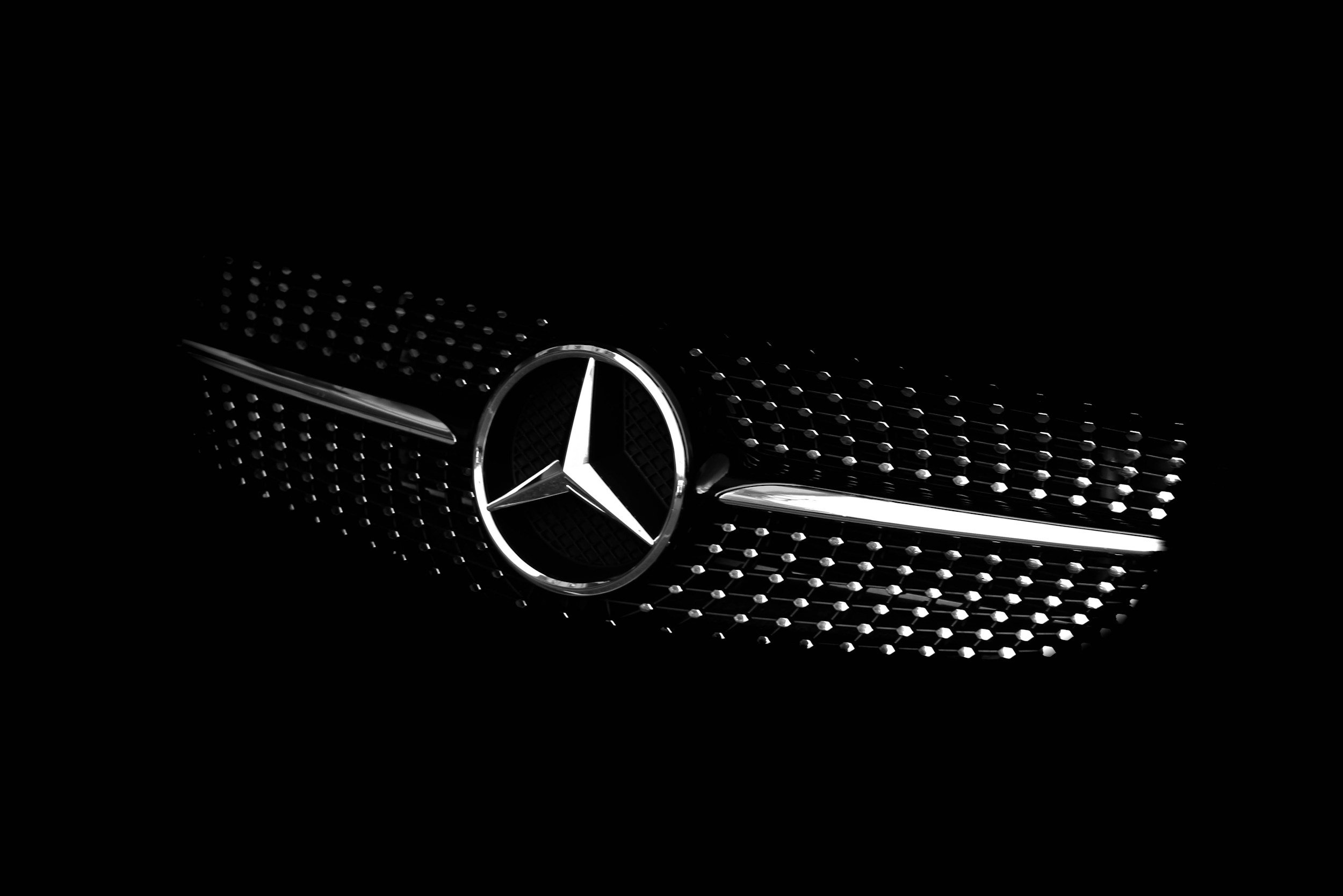 Nahaufnahme des Mercedes-Benz Logos auf der Kühlergrill eines schwarzen Autos.