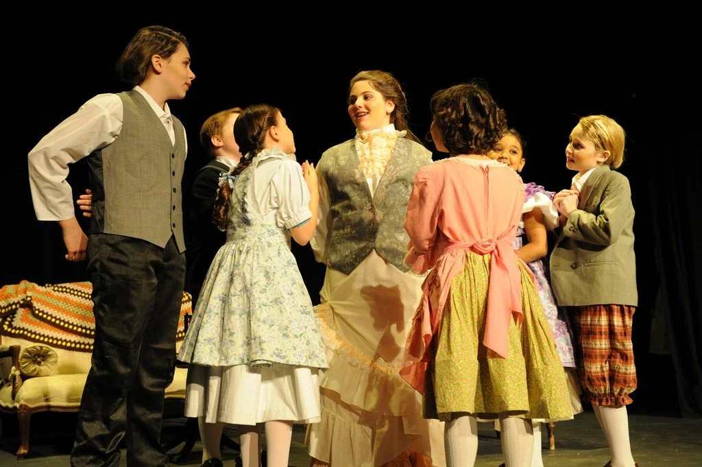 Children dressed in period costumes performing on stage in a play