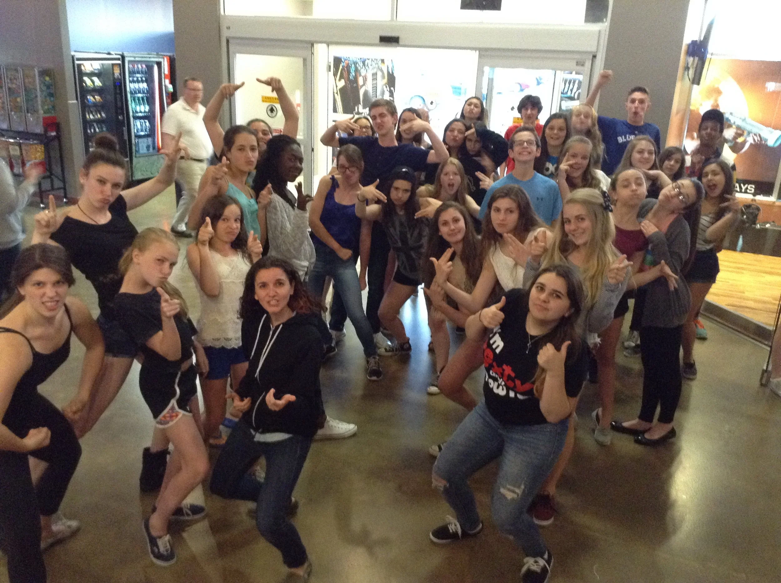 A group of teenagers gathered indoors, some posing with hand gestures, smiling and looking at the camera.