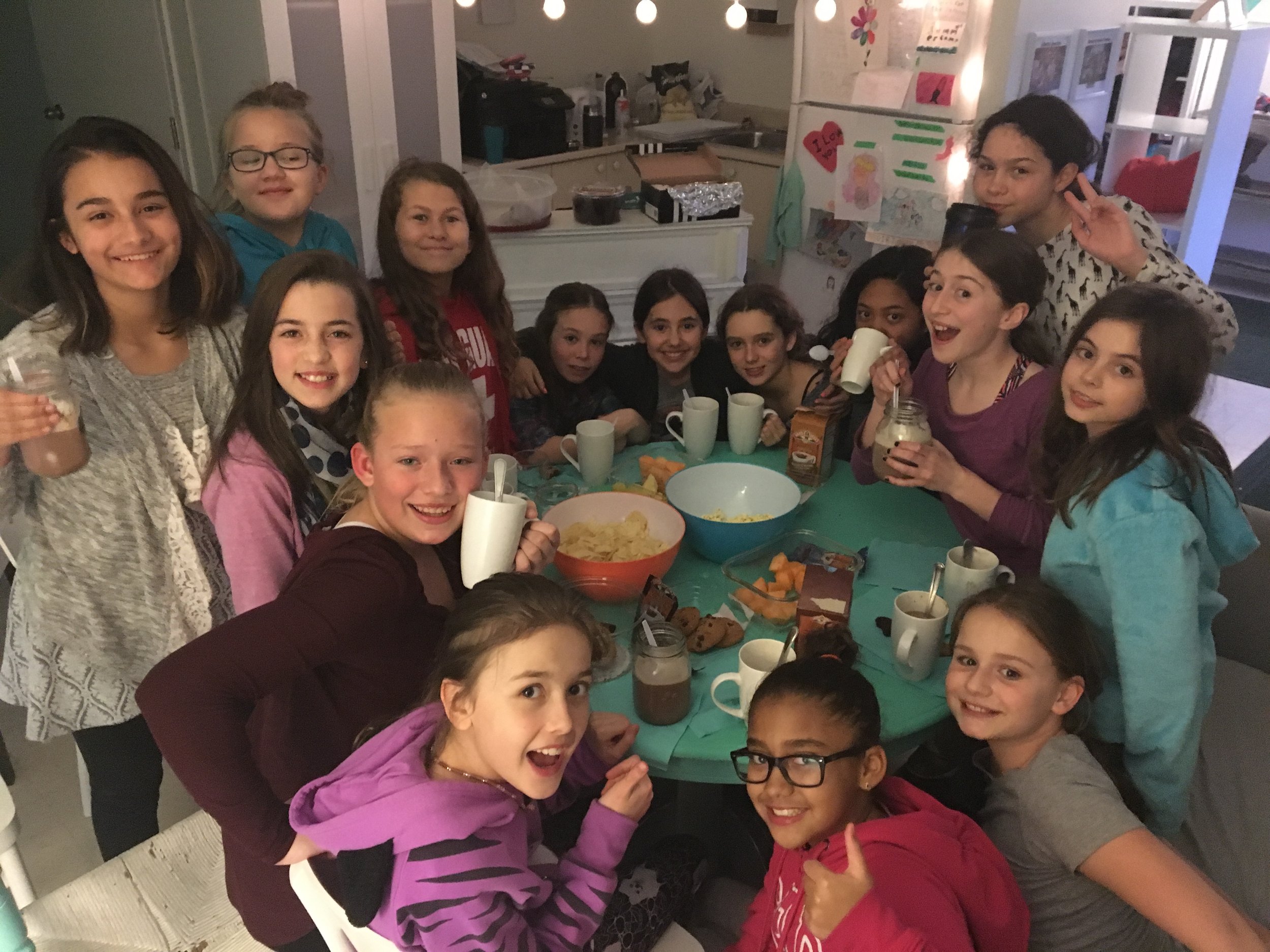 A group of children gathered around a table with snacks and drinks, celebrating together indoors.