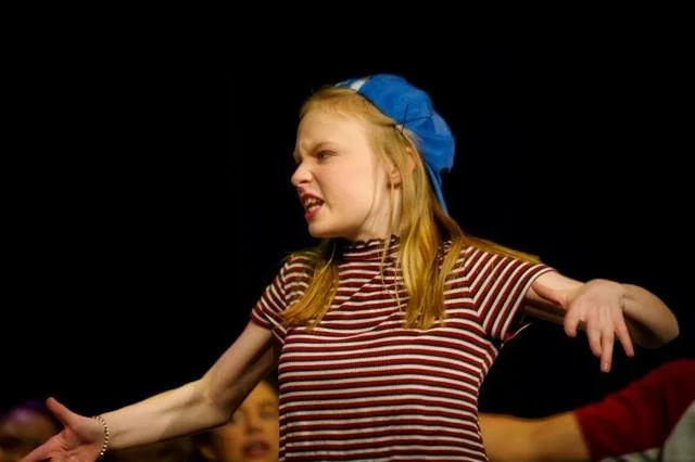 A young girl wearing a blue beret and a striped shirt appears to be acting out an angry or frustrated expression.