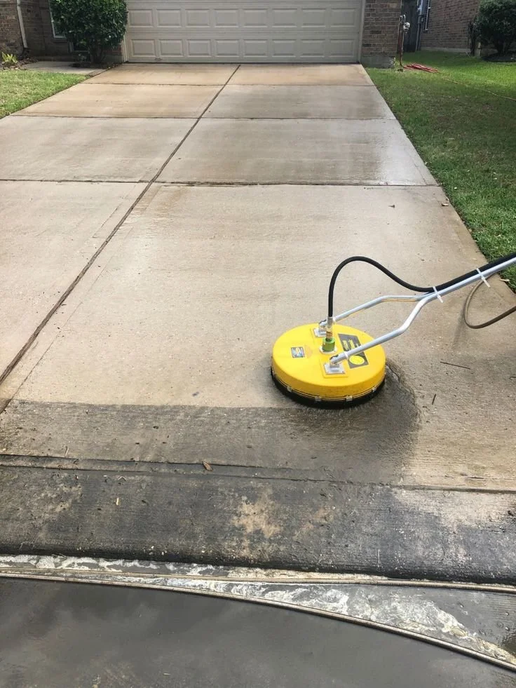 Concrete driveway being cleaned with a yellow power washer machine, with a newly cleaned section on the right and a dirtier section on the left.