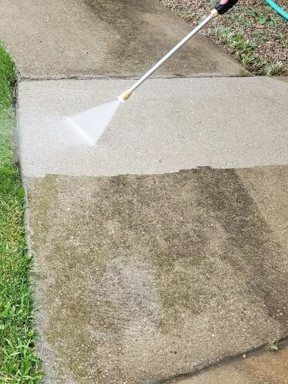 Person pressure washing a concrete sidewalk with a garden hose attachment.