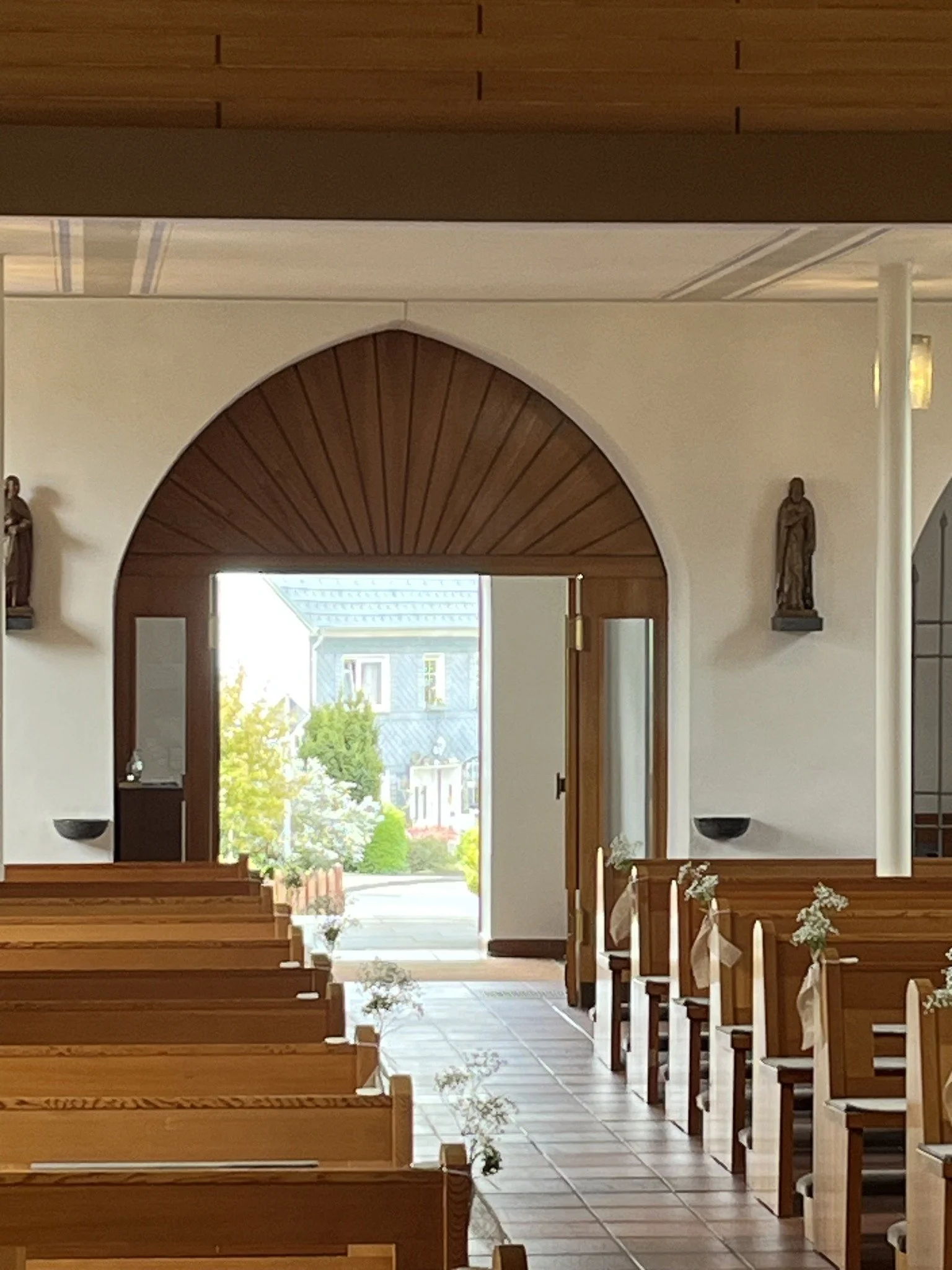 Der Eingang einer Kirche mit Holztüren, Sitzbänken und Blumenreiche Dekorationen für eine Hochzeit, Blick nach draußen auf eine Nachbarschaft mit Bäumen und Häusern.