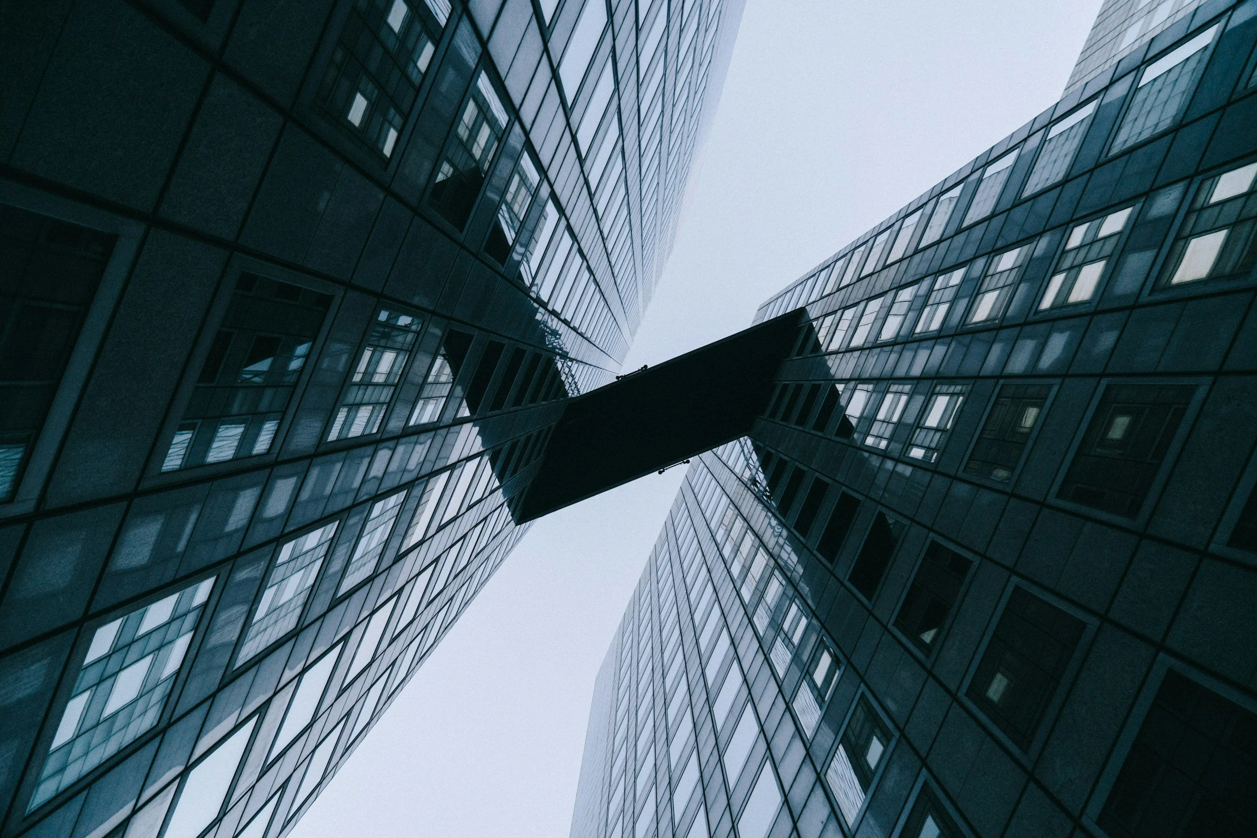 Modern glass office towers connected by a skybridge, viewed from below