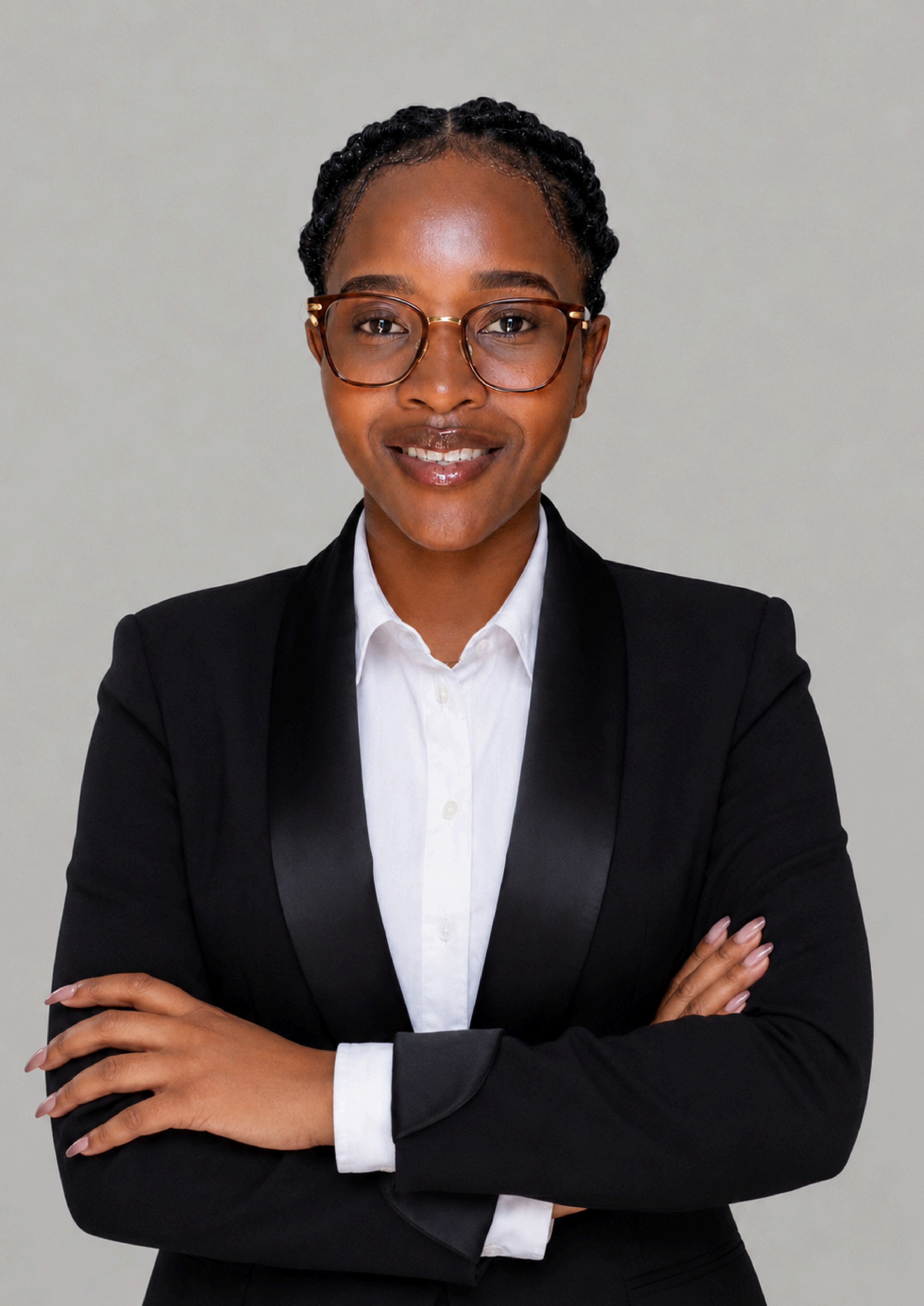 A woman with glasses in a black blazer and white shirt crossing her arms against a gray background.