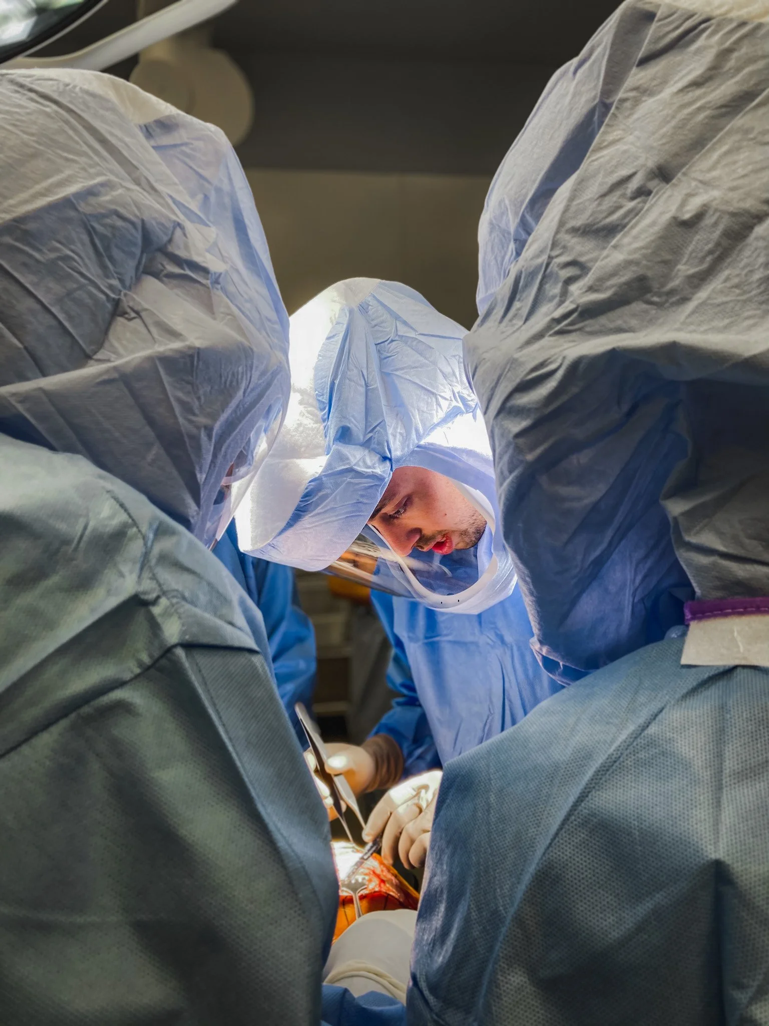 Surgeons operating in an operating room, viewed from a unique perspective between their legs.