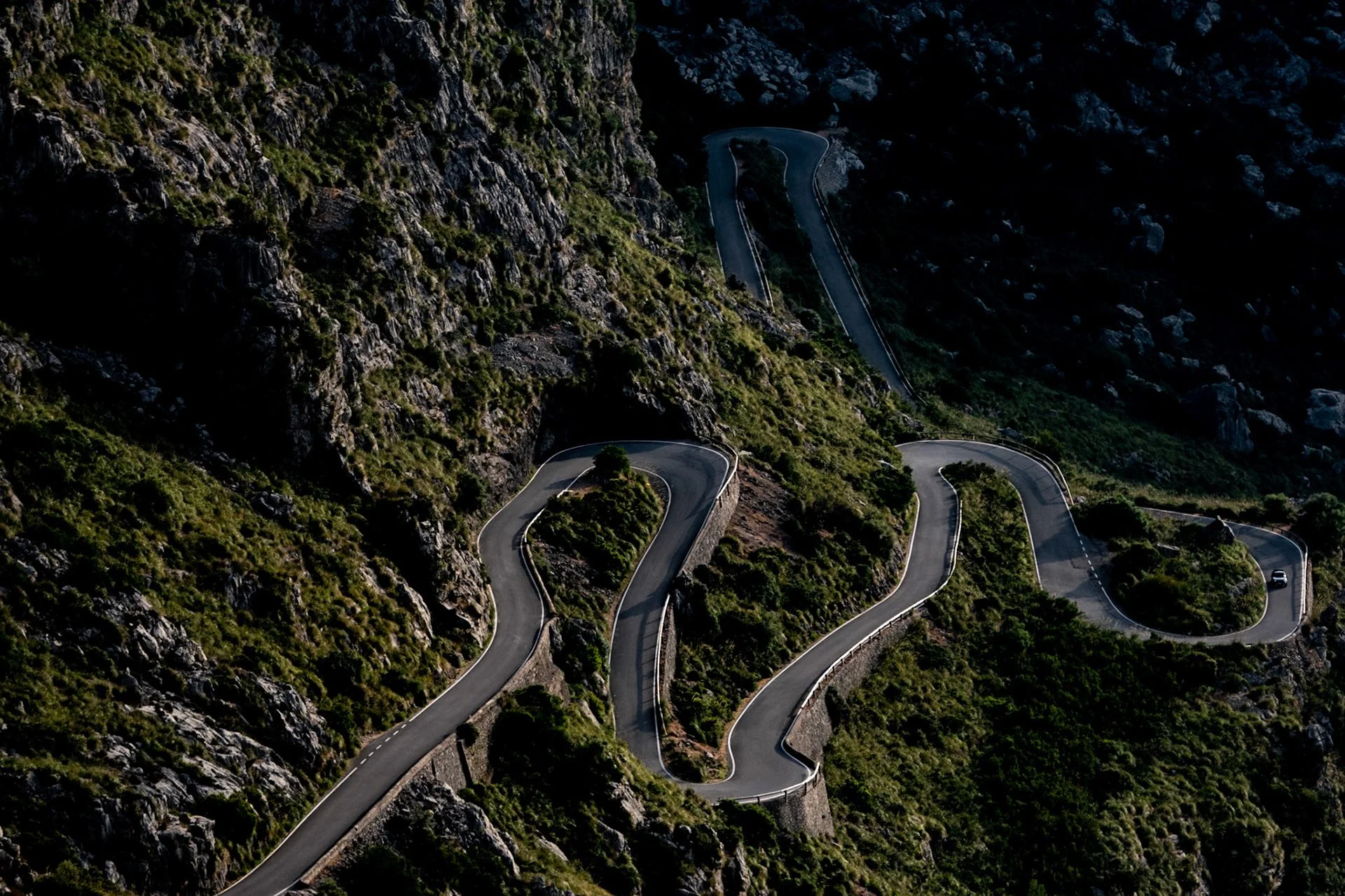 Winding mountain road with multiple sharp turns, surrounded by rocky cliffs and green vegetation.