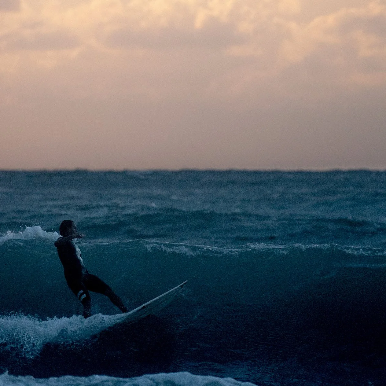 A person windsurfing on the ocean at sunset.