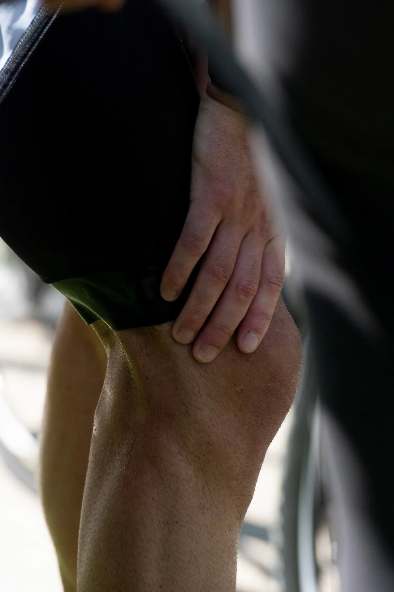 A person wearing black pants and a black shirt with a hand resting on their thigh.