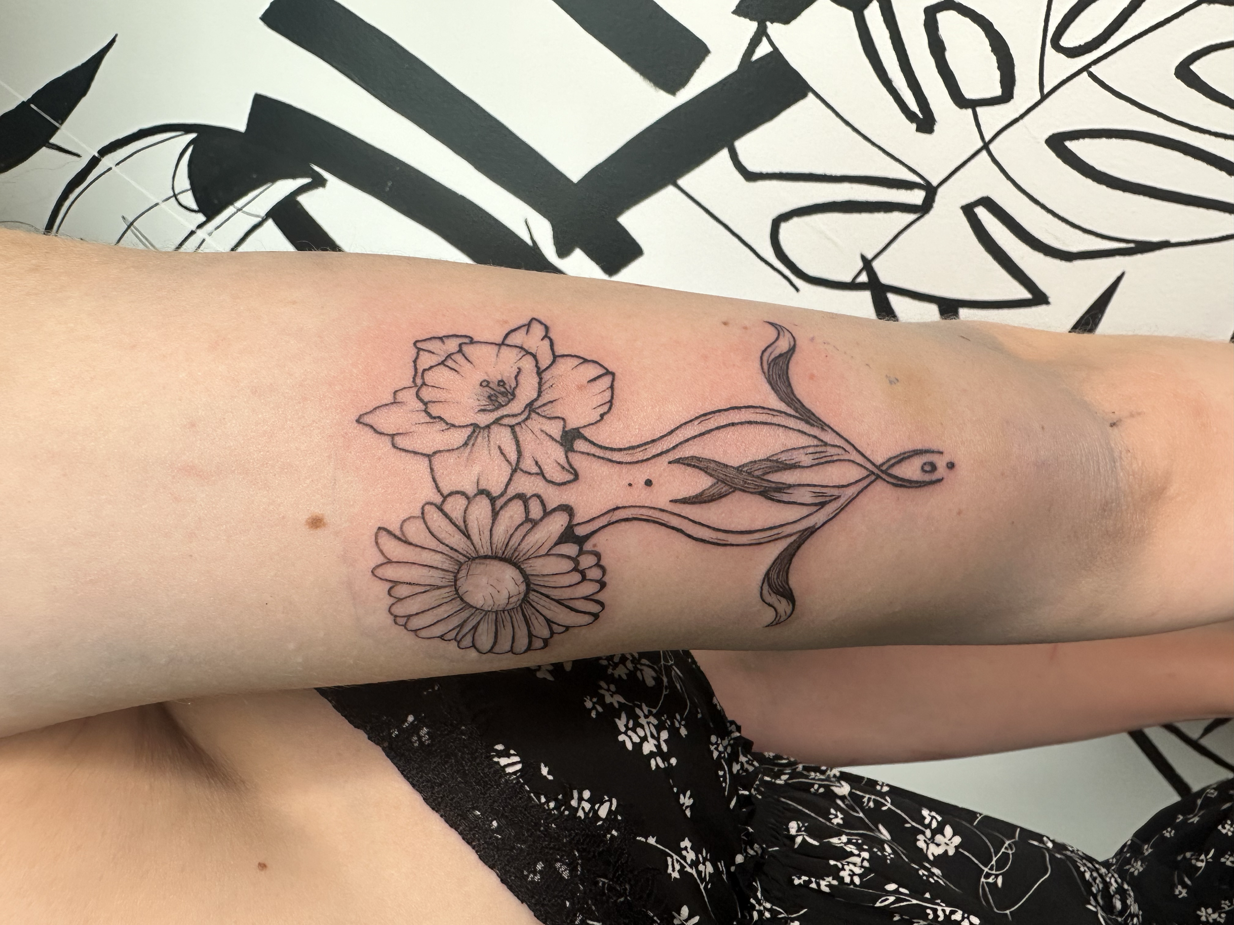 Tatouage de fleurs sur un bras, avec des lignes noires dessinant des fleurs et des feuilles.