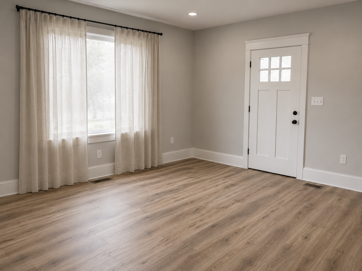 Empty room with light wood flooring, a window with cream curtains, and a white door with a small window at the top.