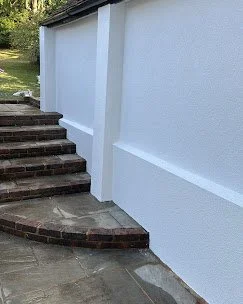 Close-up of a white exterior wall with brick steps and a concrete patio in front.