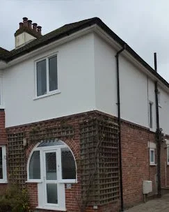 The upper part of a two-story house with white exterior walls and a chimney on the roof.