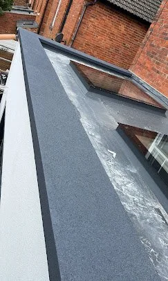 Close-up of a glass roof with water and dirt stains, attached to a brick building.