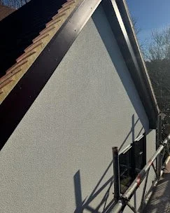 A portion of a building roof with a sloped surface, shingles, and a blue sky in the background.