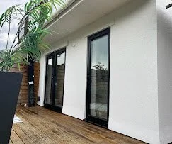 Exterior of a modern building with large glass doors and windows, a wooden deck, and a palm tree.