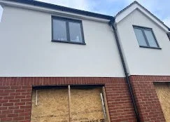 Part of a two-story house with a boarded-up garage door, brick on the first floor, and white siding on the second floor.