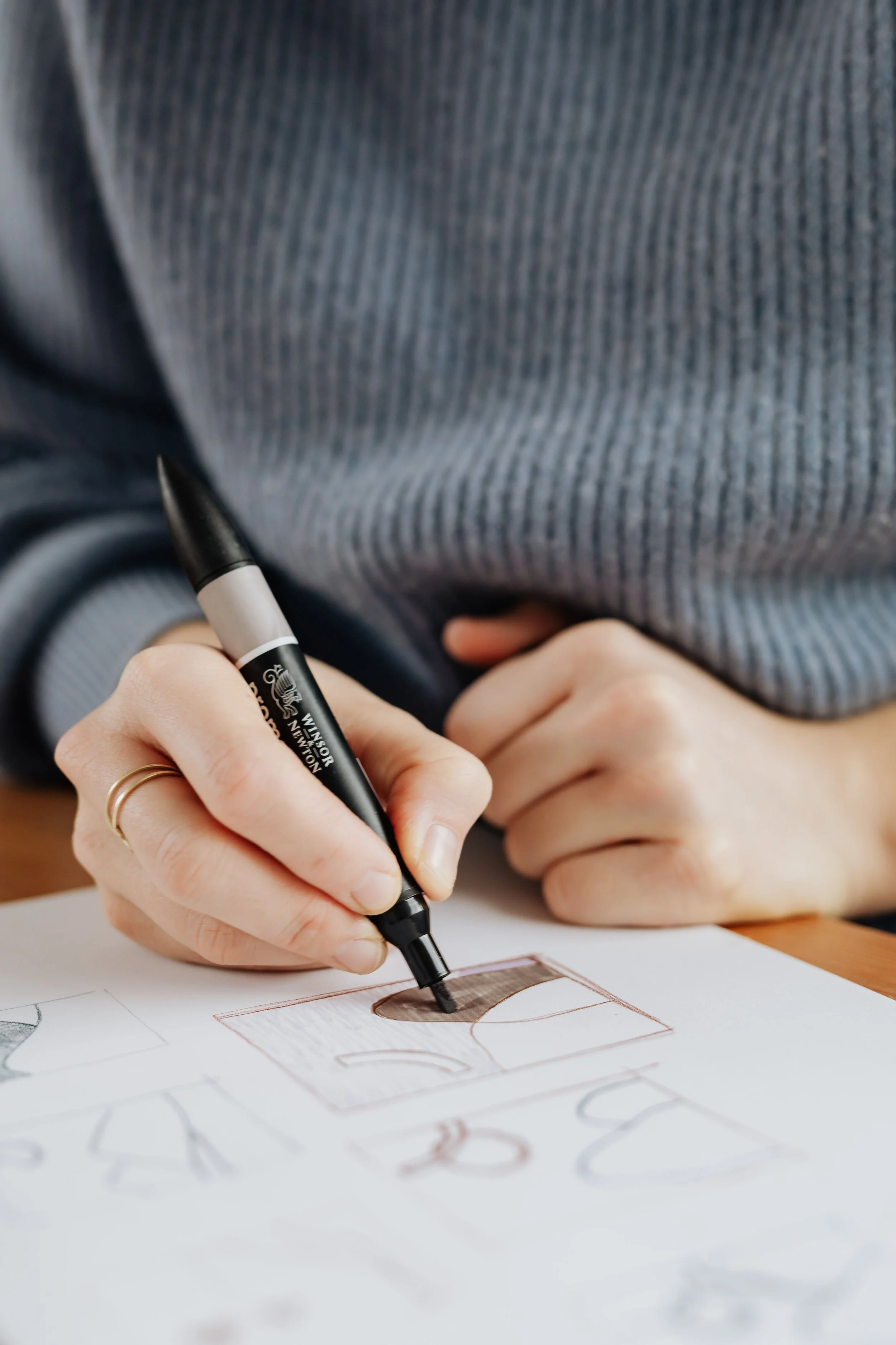 A person using a black marker to color in a drawing on a piece of paper, wearing a gray striped shirt.
