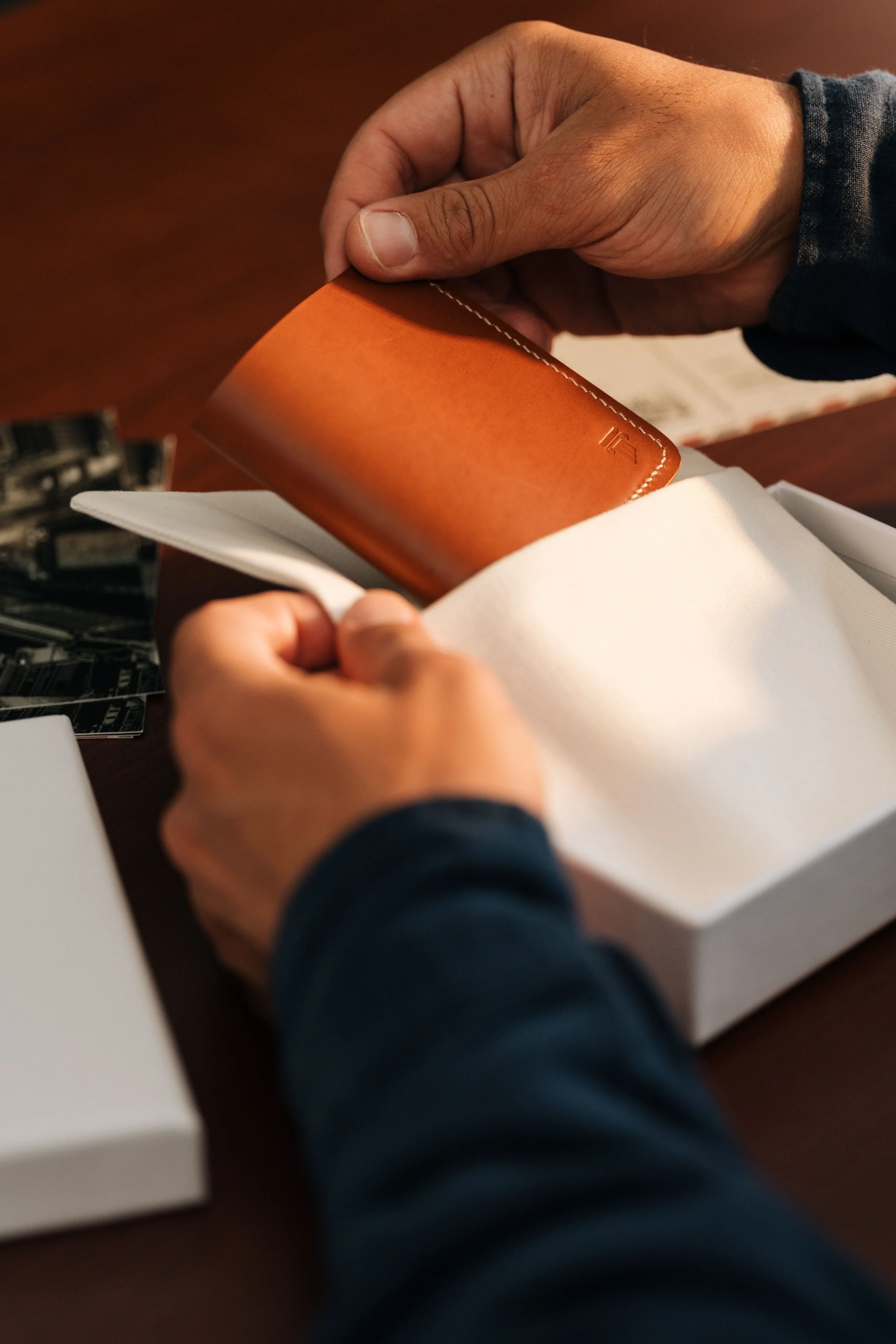 A person holding an orange leather wallet over a white box on a wooden table.